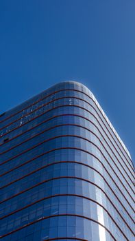 Contemporary glass skyscraper rises against a clear blue sky, showcasing urban architecture.