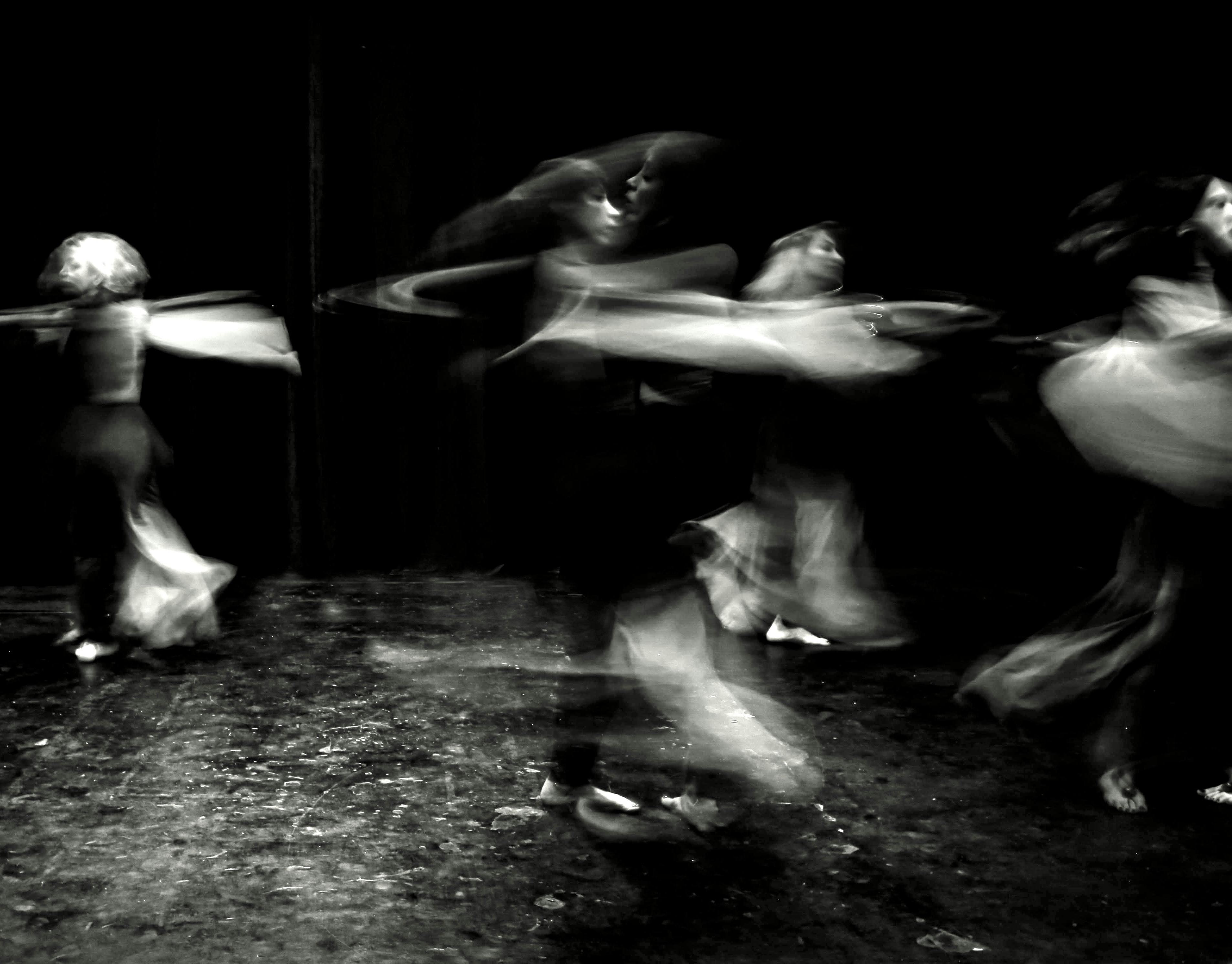 Black and white image capturing dancers in motion on stage, creating an abstract blur effect.