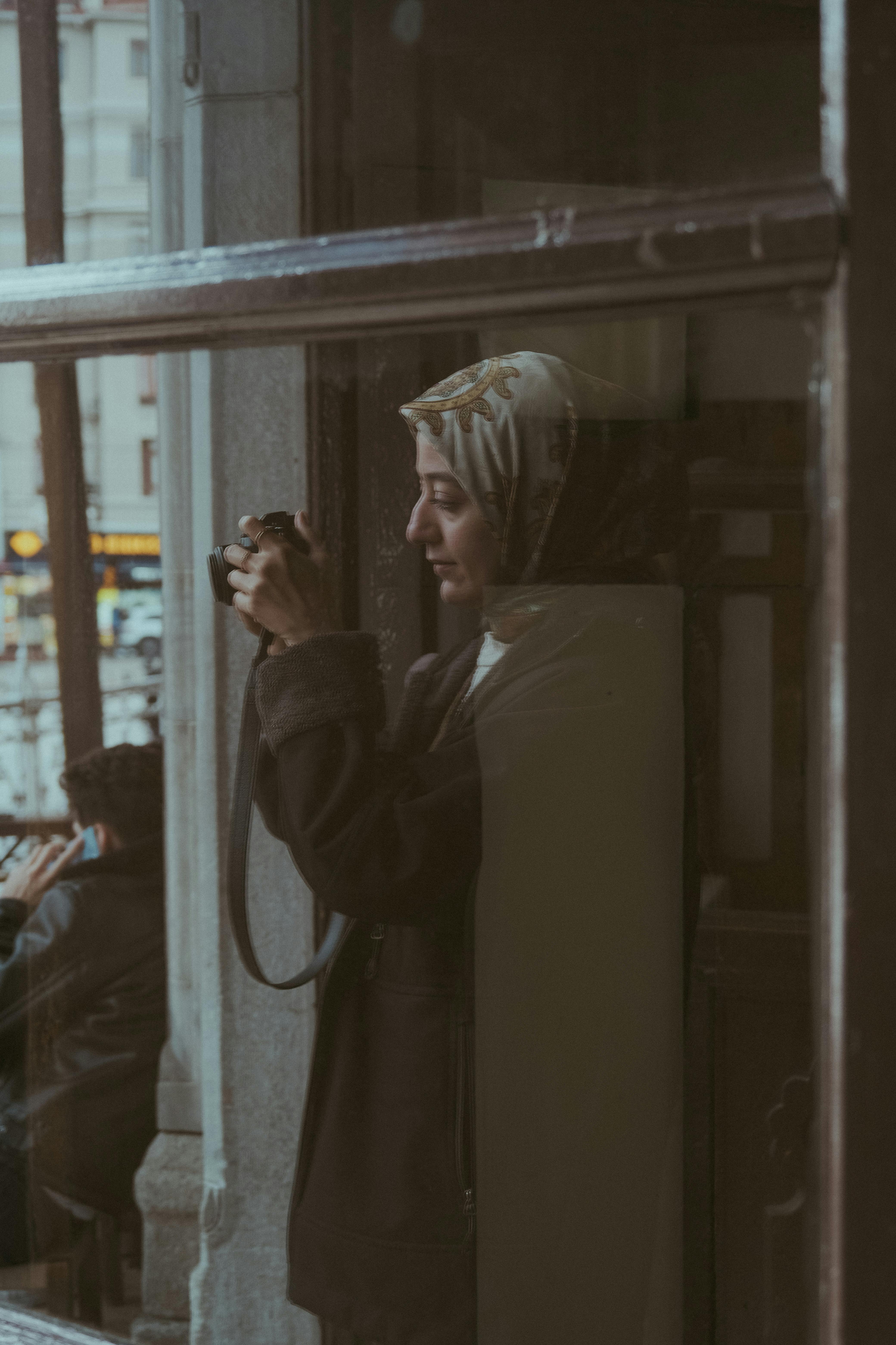 grátis Captura reflexiva de uma mulher tirando fotos através de uma janela em um ambiente urbano. Foto profissional