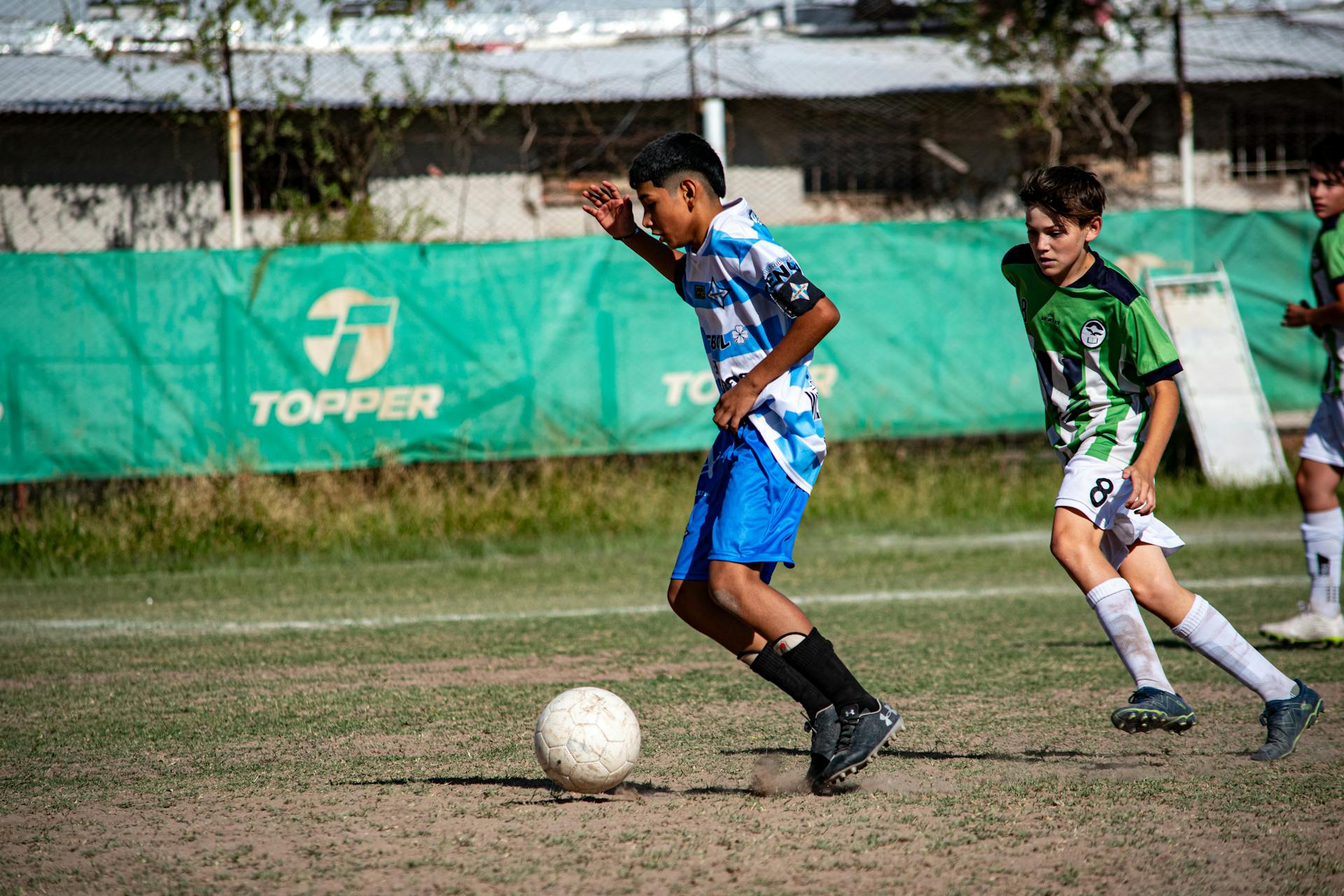 Exciting youth soccer match with kids dribbling at summer outdoor field.