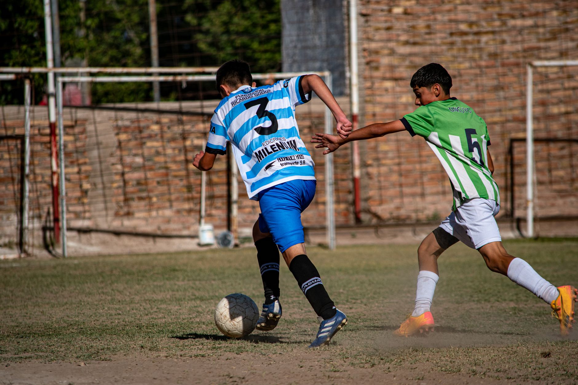 three youth football players competing in a tight small-sided game under bright evening floodlights