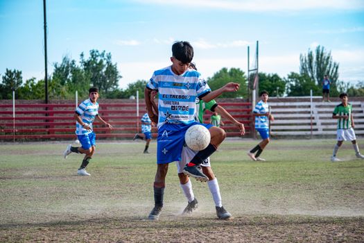 Young soccer players compete intensely on a dusty outdoor field during the day.