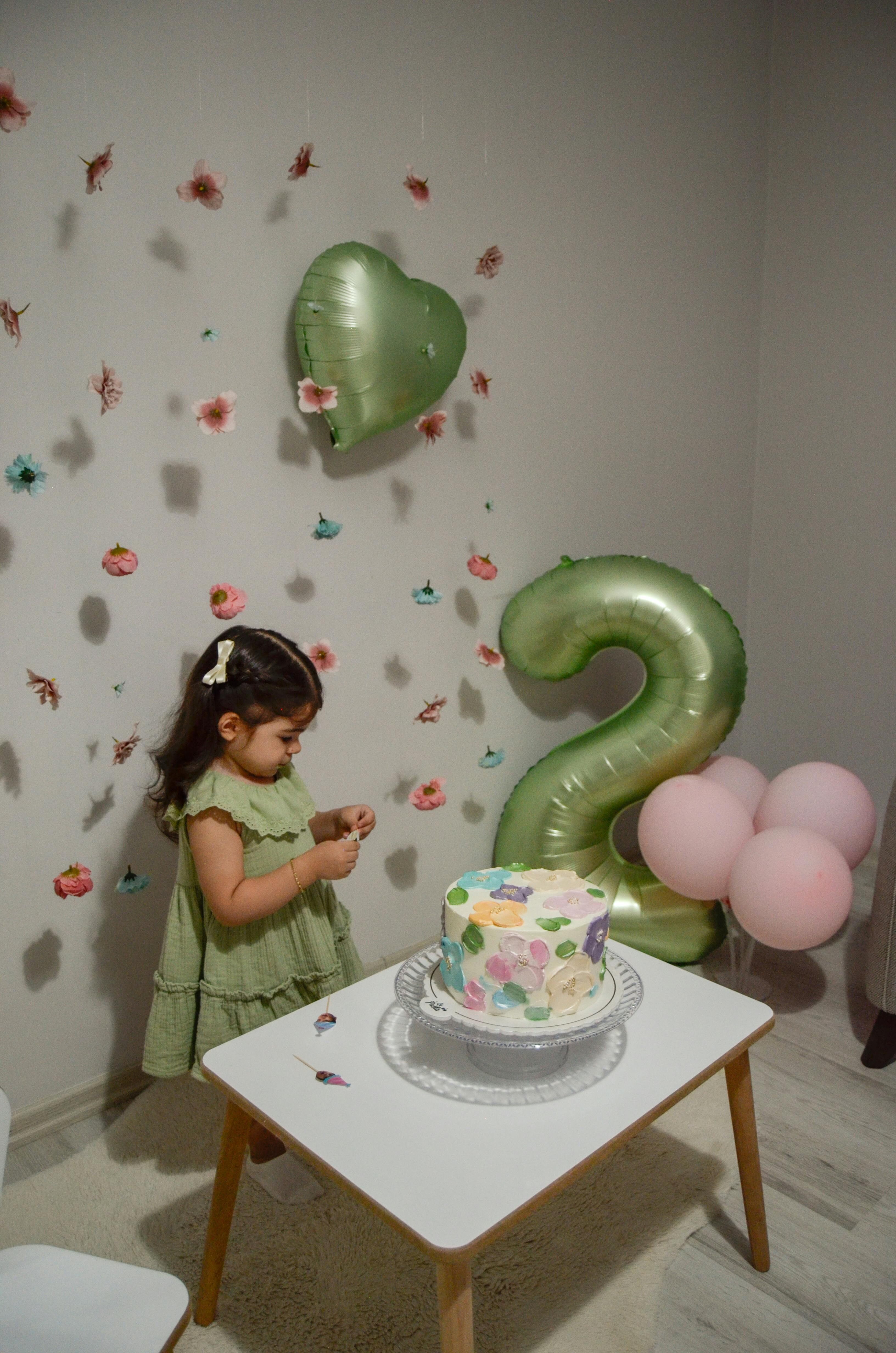 Adorable toddler celebrating second birthday with balloons and cake indoors.