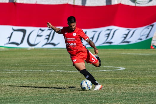 Action-packed moment of a soccer player in red during a competitive match on a green field.