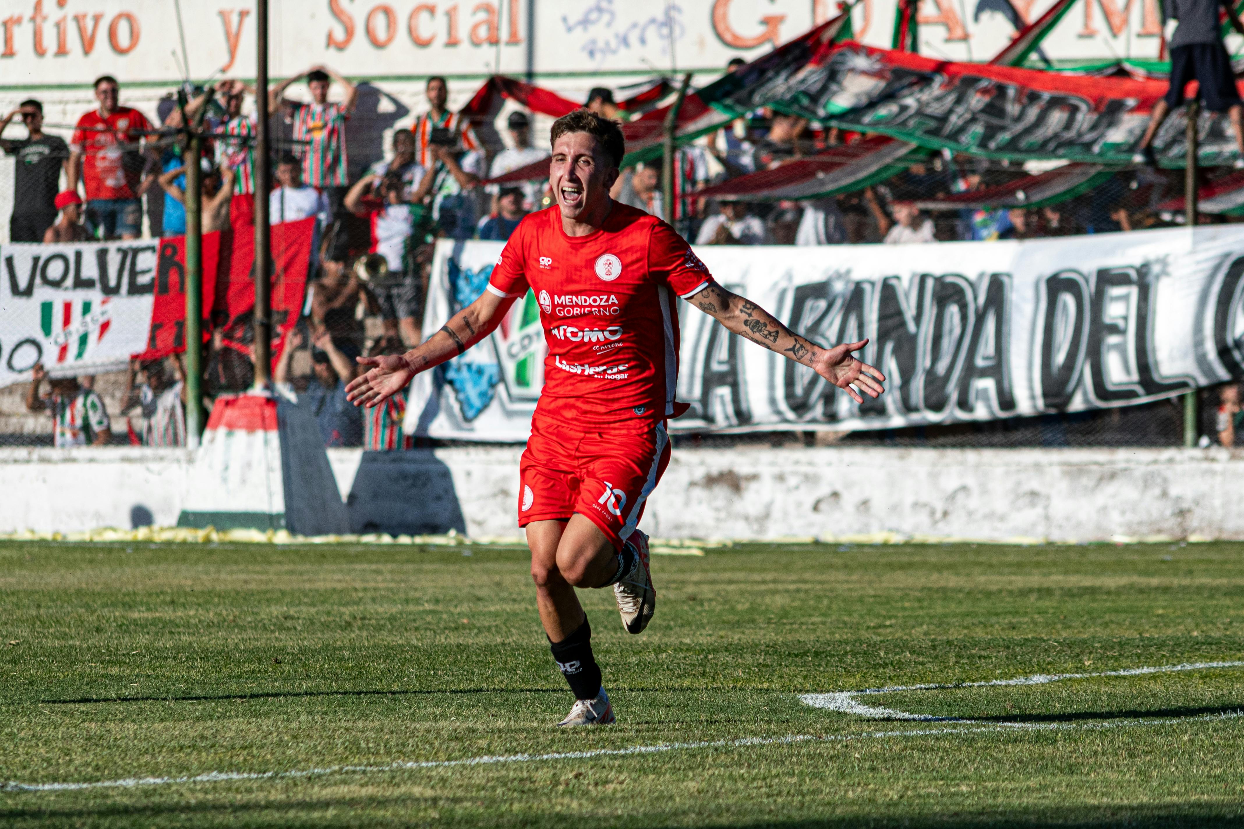 Excited soccer player celebrates scoring a goal with cheering fans in background.