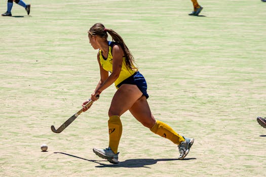 Focused female field hockey player in motion on a sunny day.