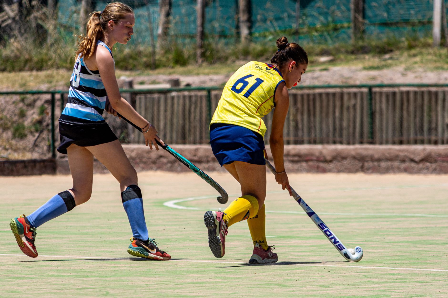 Two female athletes competing in an intense field hockey match outdoors.