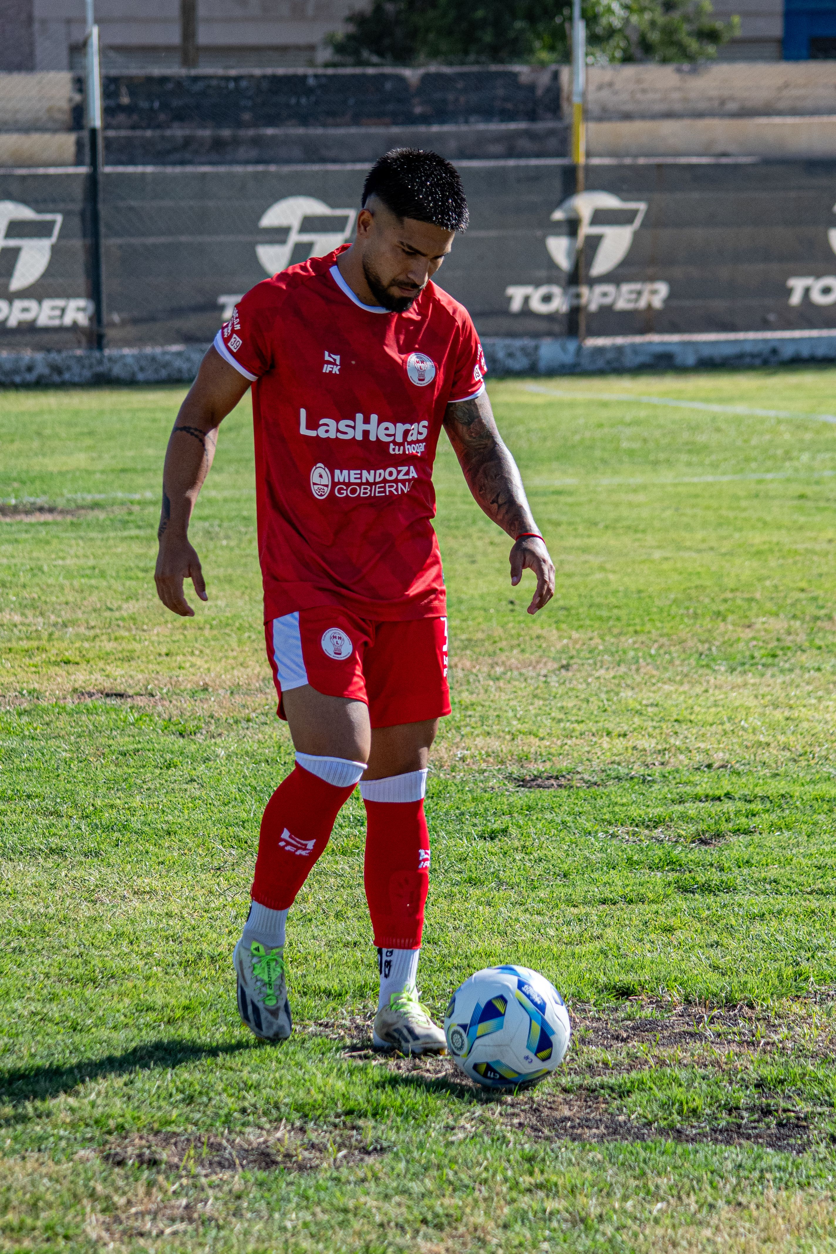 Soccer player in red team uniform about to kick a ball on a field.