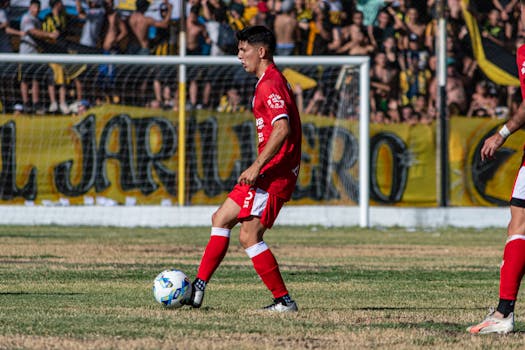 Soccer player in red kit controlling the ball during a vibrant outdoor match.
