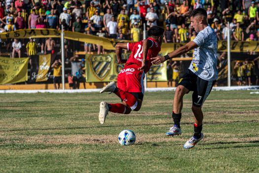 Two soccer players in action on a field, with a vibrant crowd in the background.