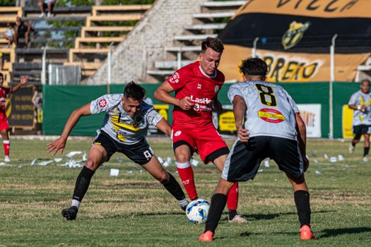 Action-packed soccer game between teams in red and black uniforms on a sunny outdoor field.