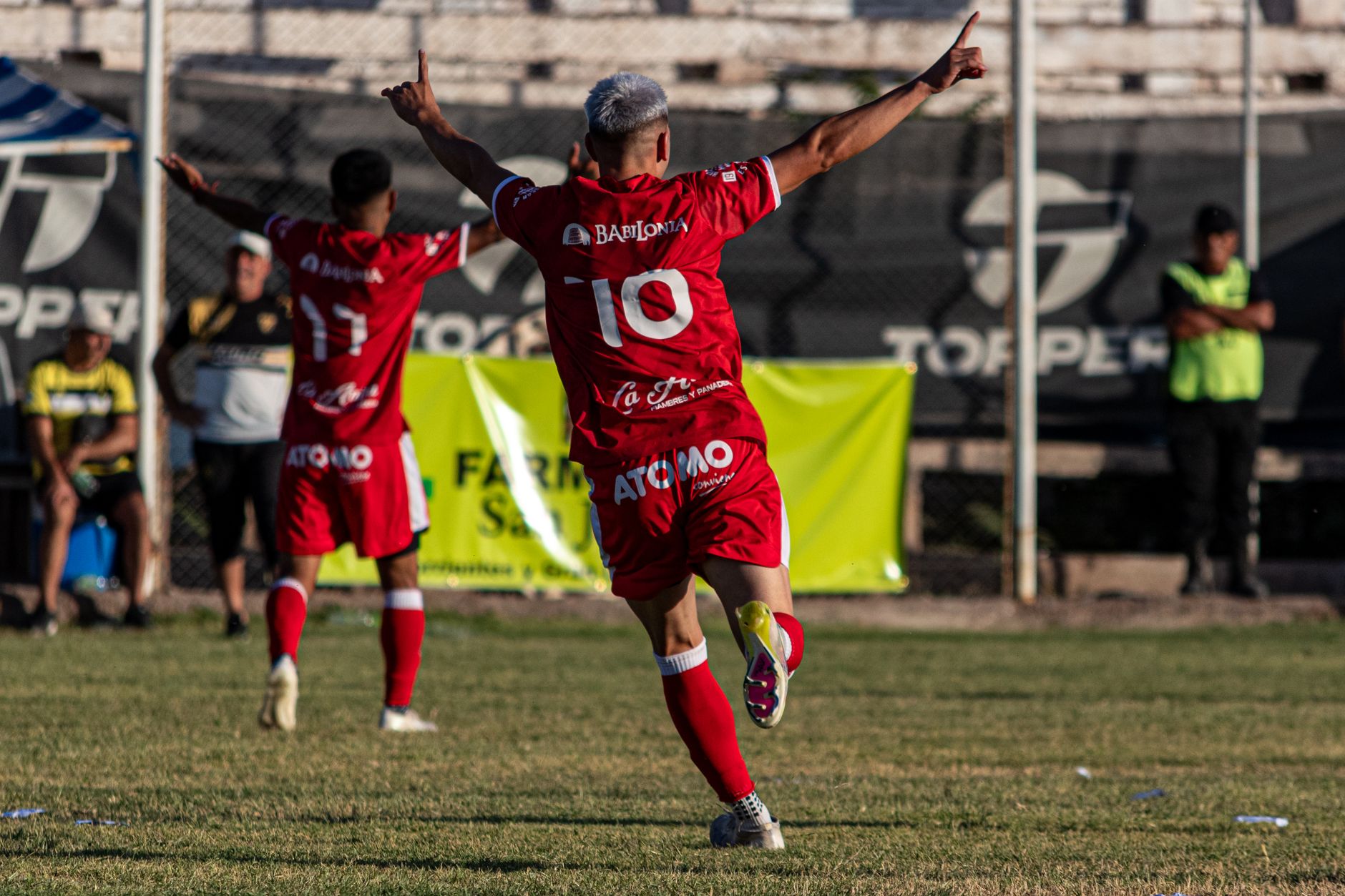 Soccer players in red jerseys celebrate a goal during a match under a sunny day.
