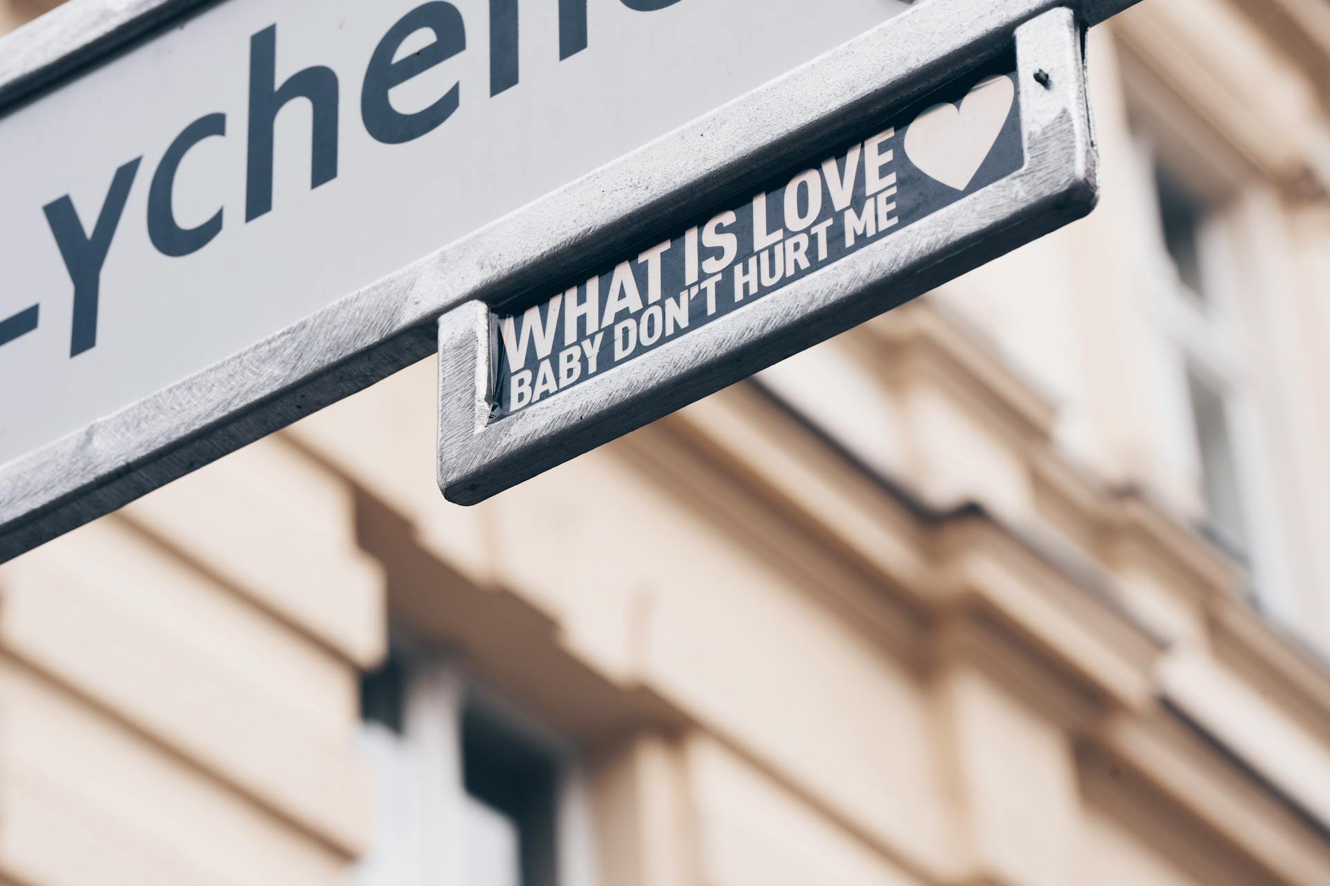 Street sign displaying 'What is Love' quote with heart icon in cityscape background.