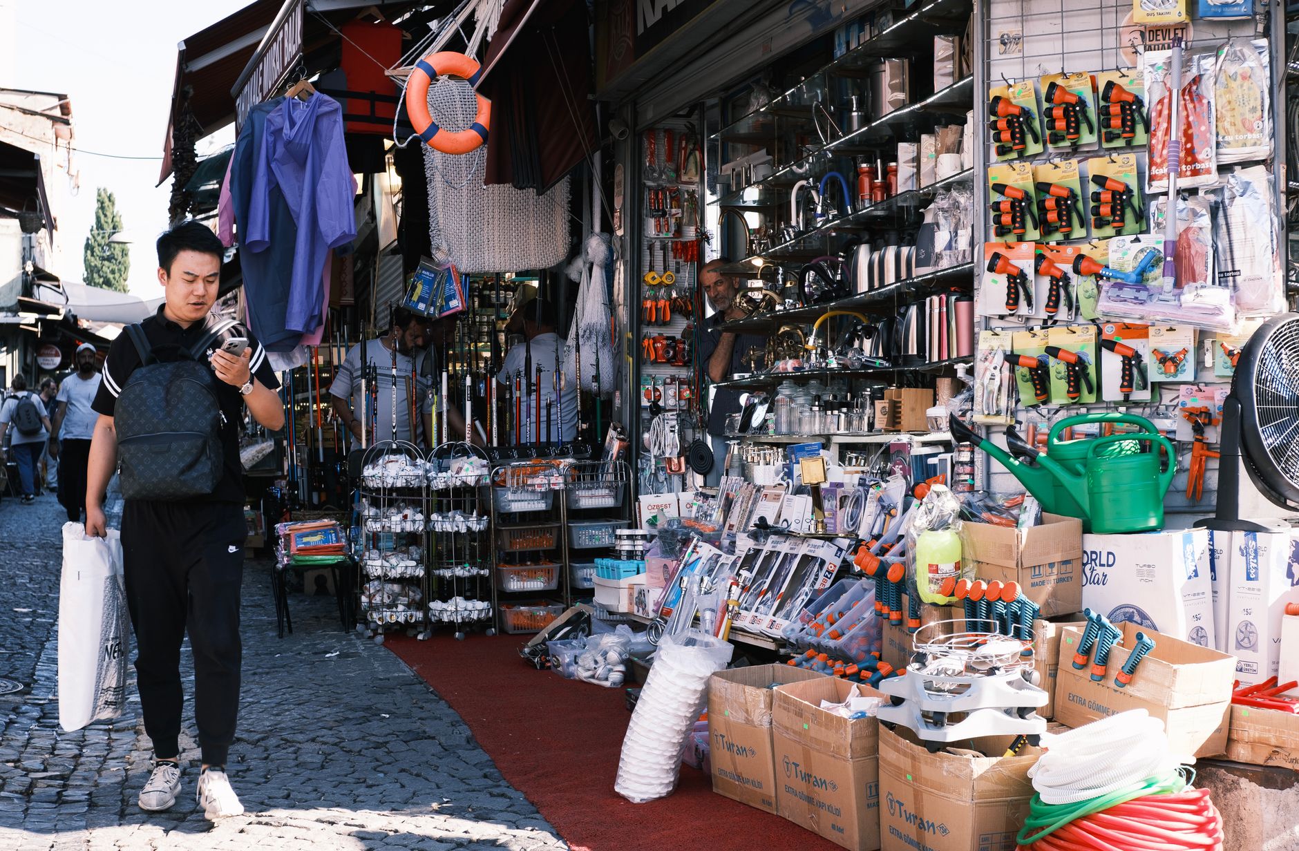Man browsing tools at a vibrant outdoor market stall offering diverse hardware products.