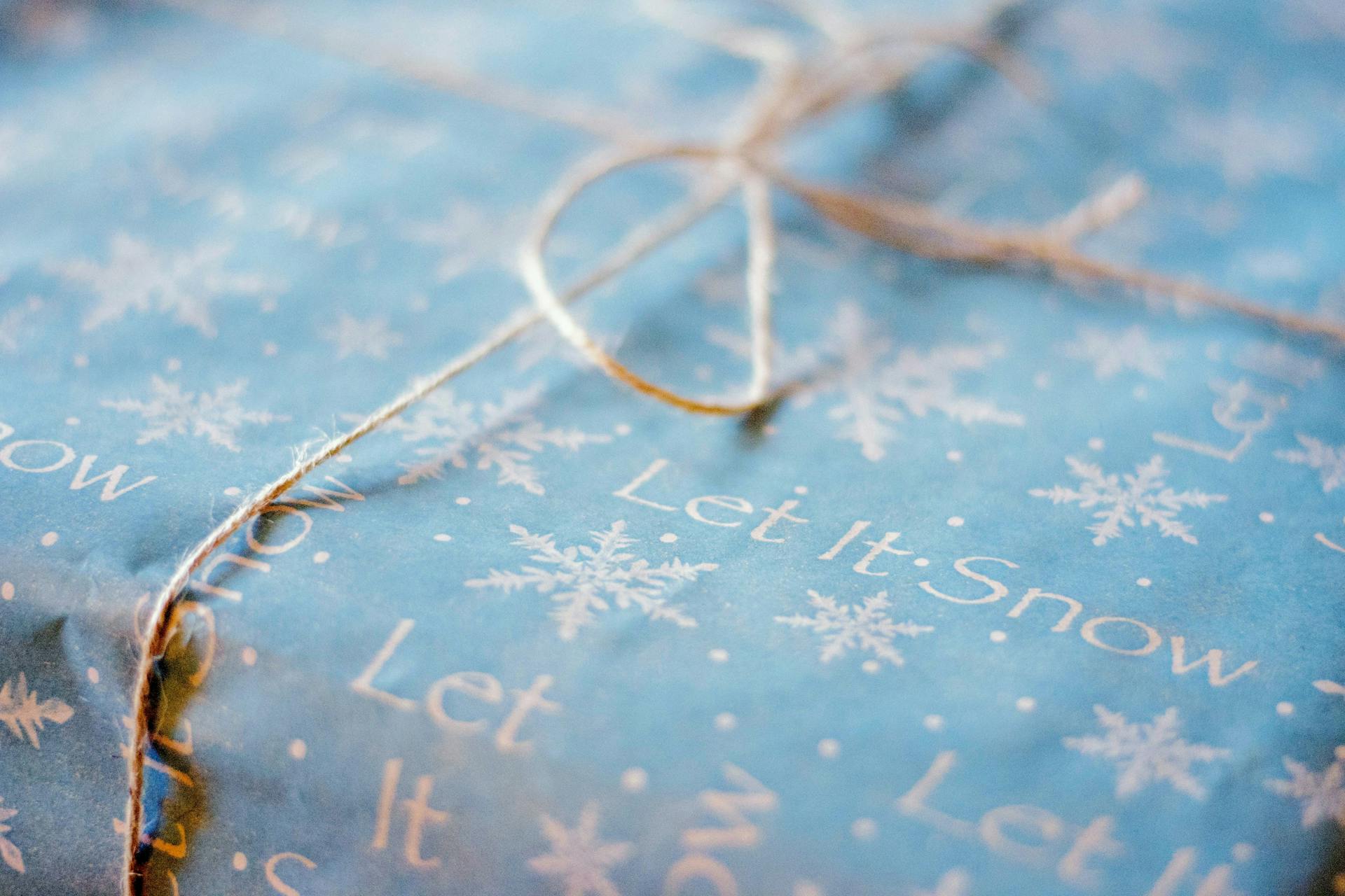 Close-up of a gift wrapped in blue snowflake-themed paper with 'Let It Snow' text, perfect for winter holidays.