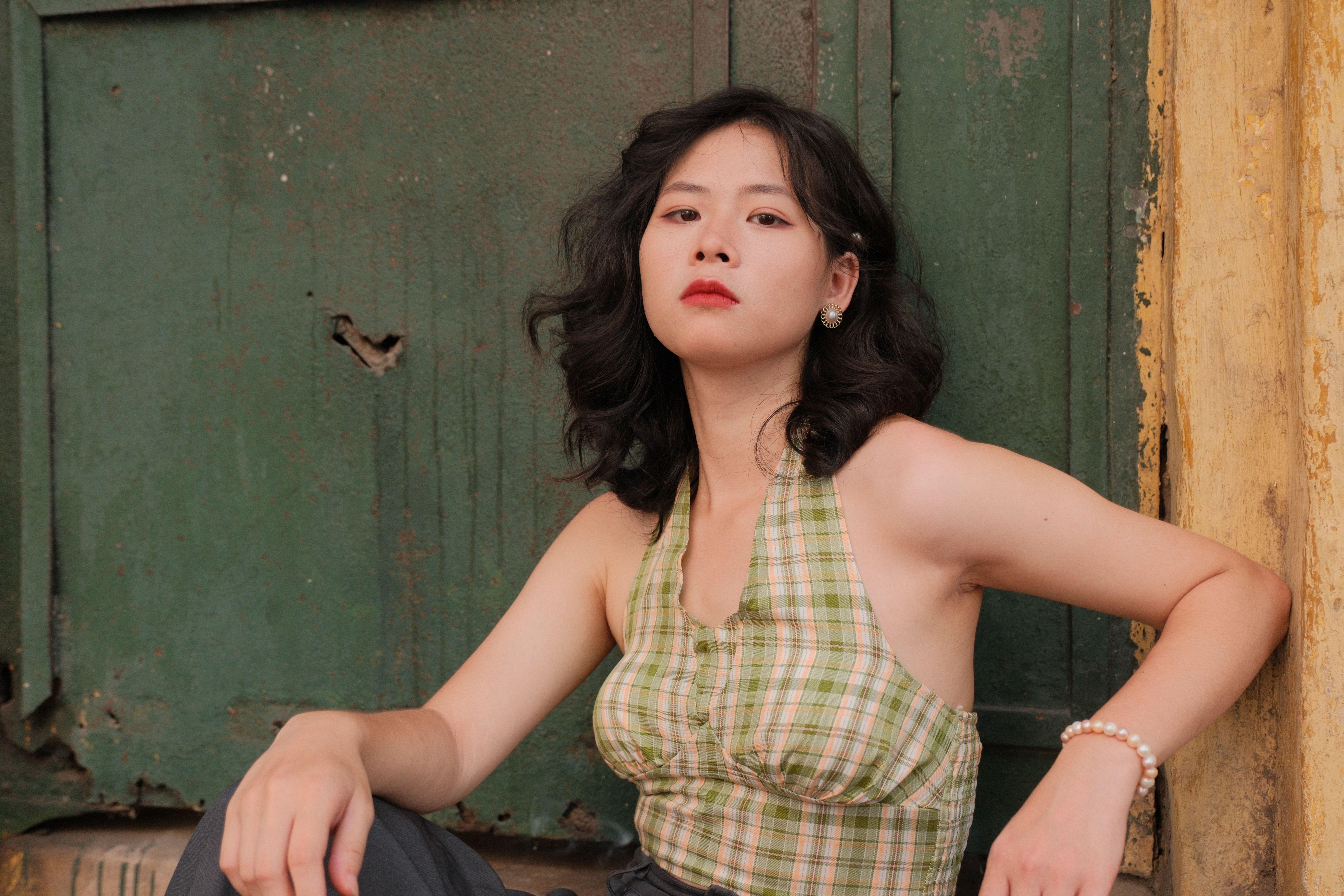 Confident woman in plaid top posing outdoors against a rustic green door.