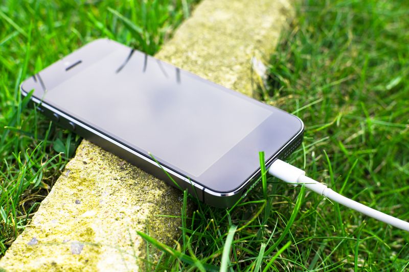A smartphone with a charging cable rests on grass outdoors, showcasing modern technology in nature.