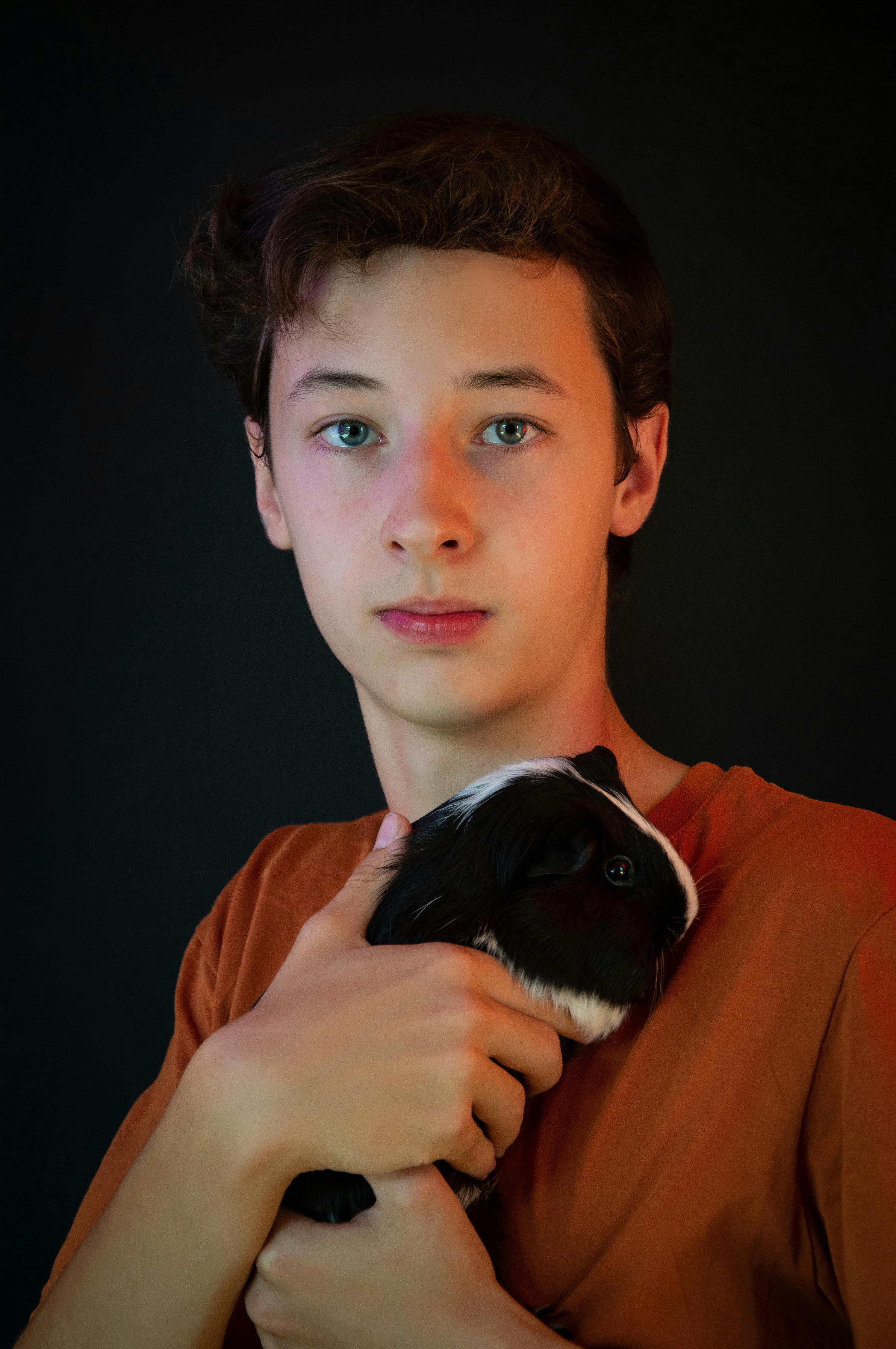 Miễn phí Người trẻ đang cầm một con chuột lang trên nền tối. Ảnh lưu trữ