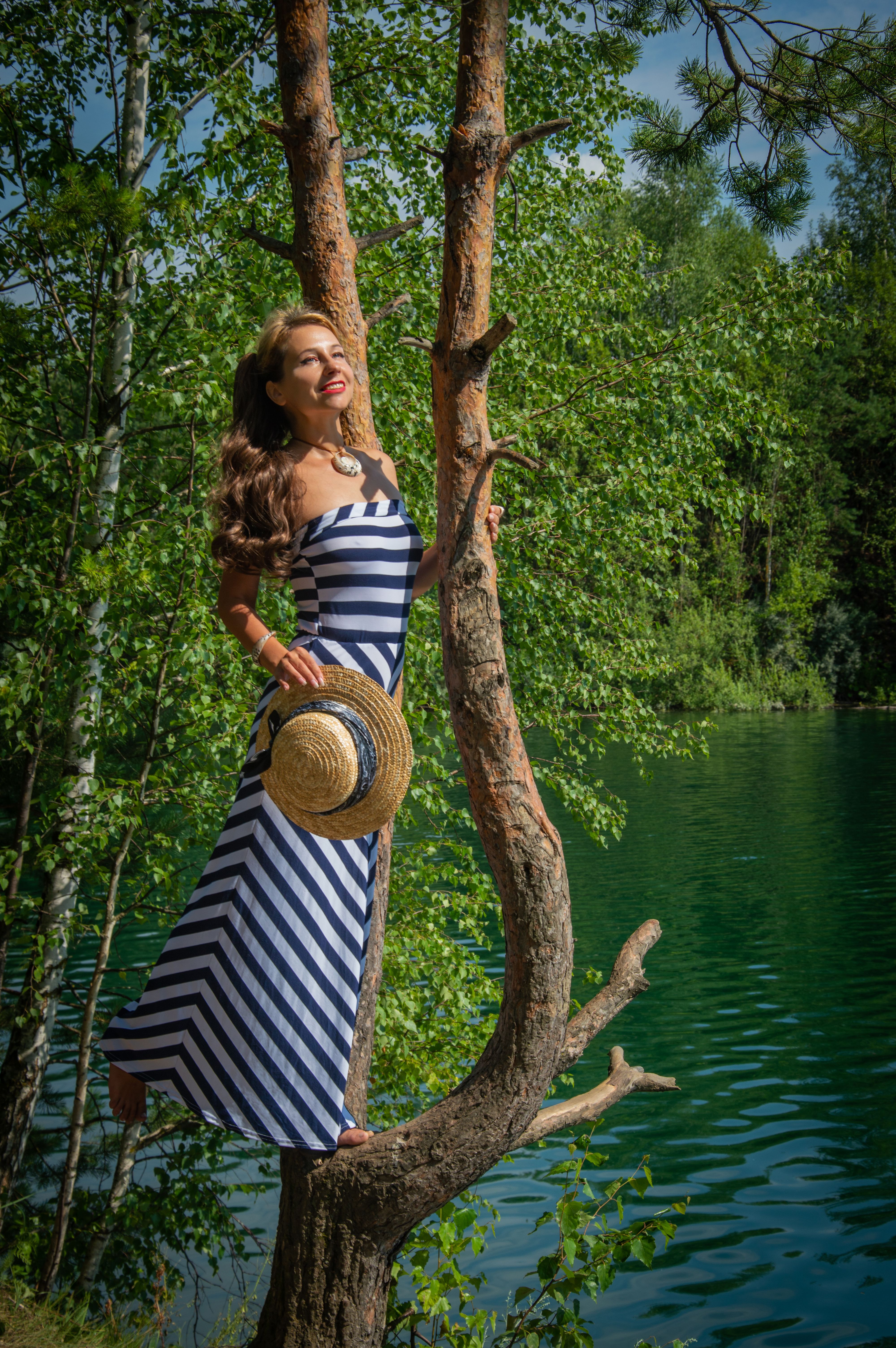 Woman in striped dress posing on tree by lake · Free Stock Photo