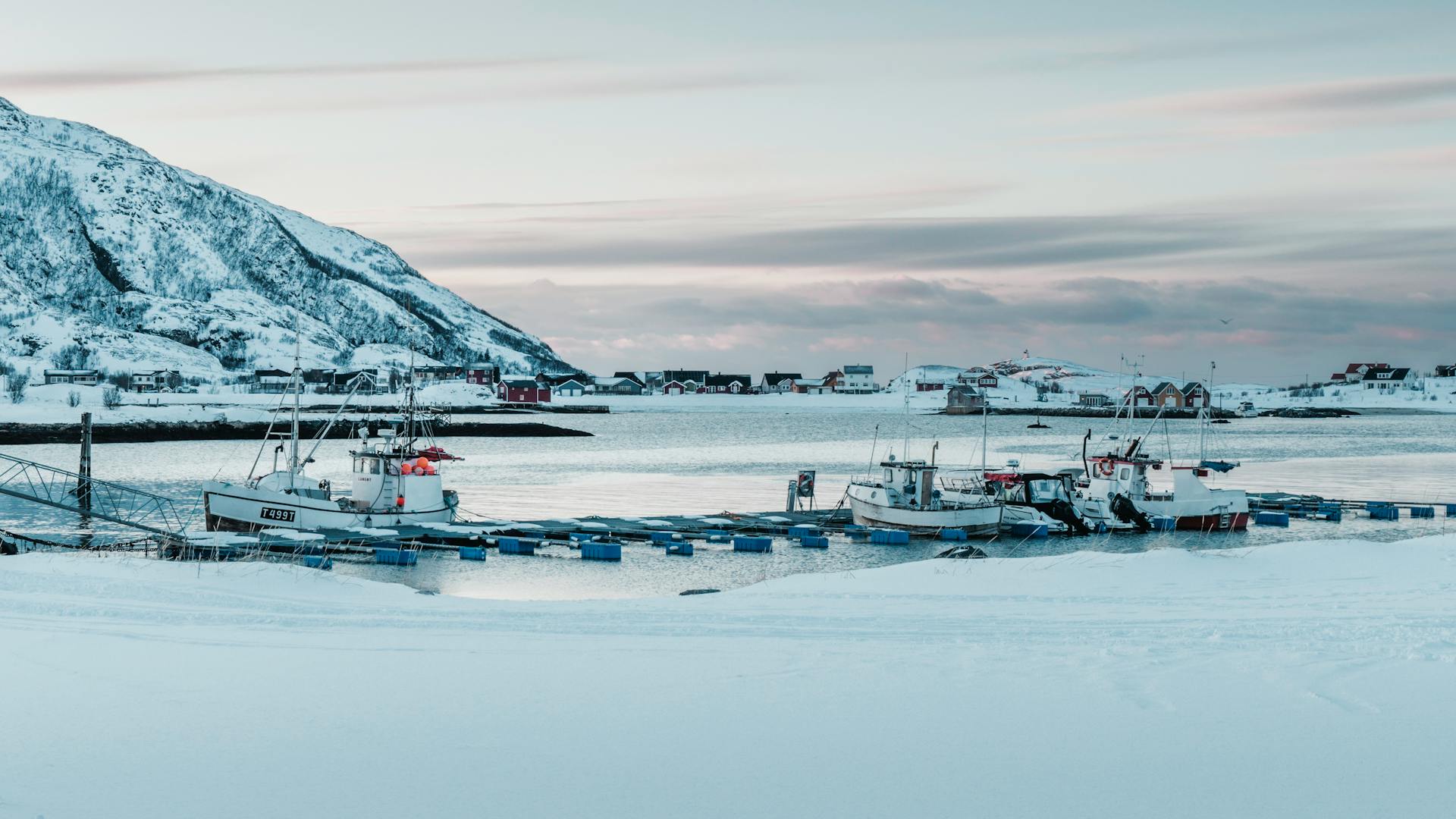 Snow-covered harbor with boats against a picturesque Norwegian winter backdrop.