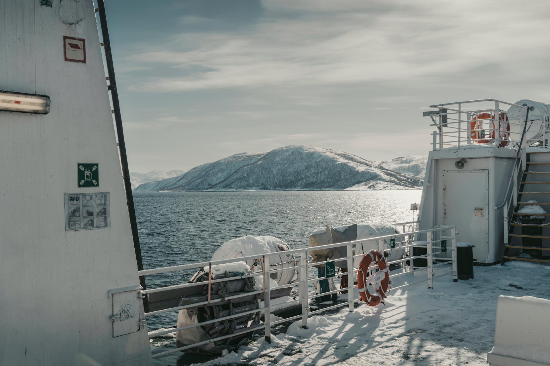 Winter landscape from a ferry in Norway with snow-covered mountains and calm sea.