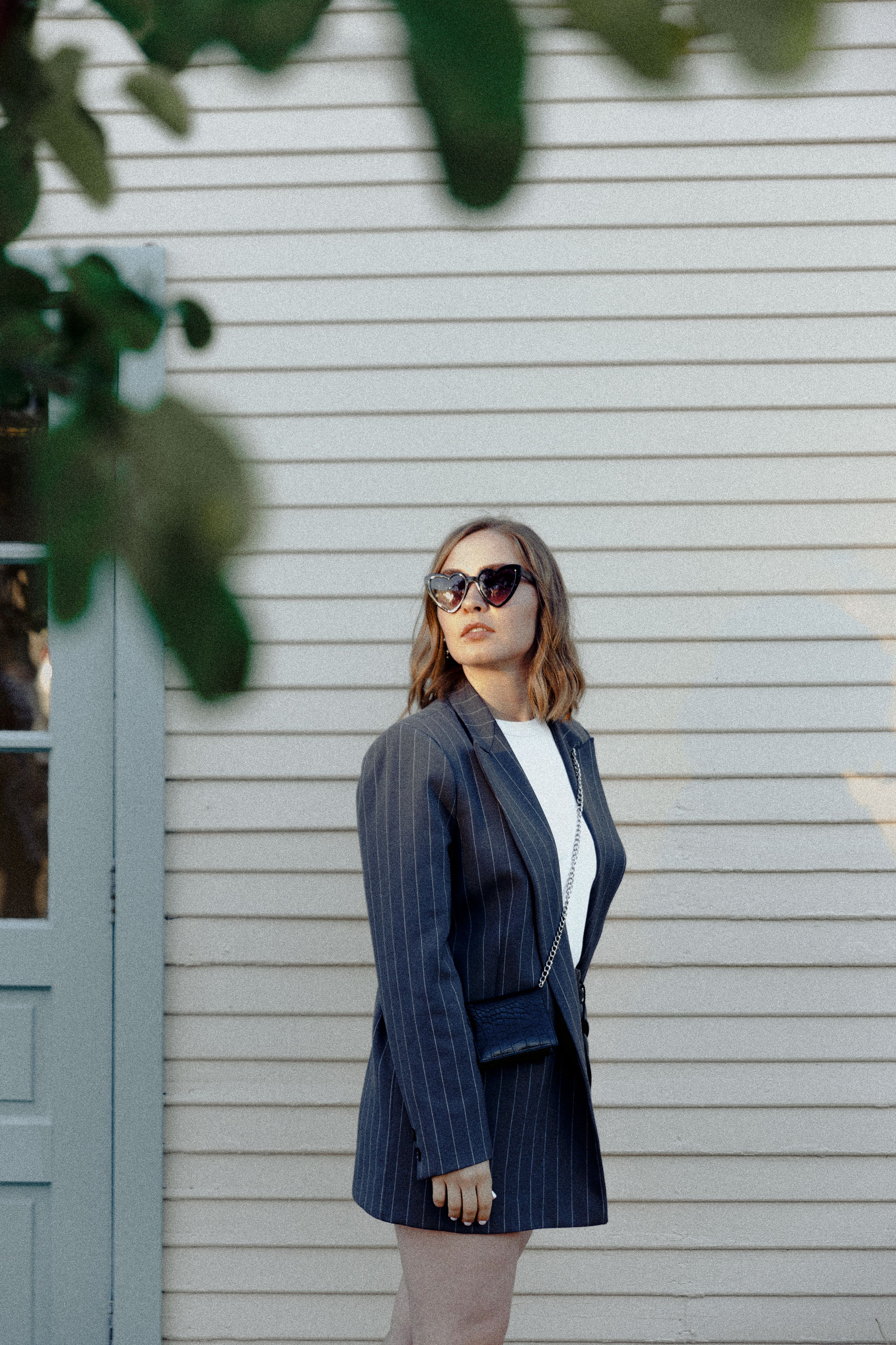 Mulher estilosa de óculos de sol e blazer listrado posando com confiança do lado de fora de um prédio.