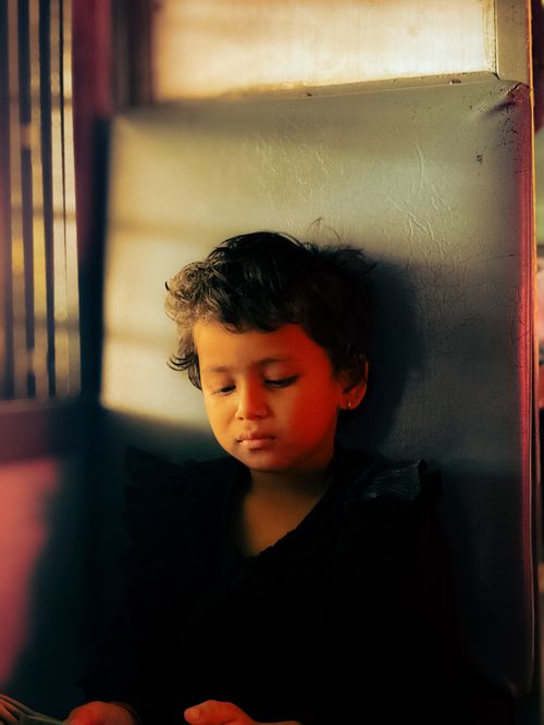 Free A young child reads quietly, bathed in warm sunlight indoors with a contemplative expression. Stock Photo
