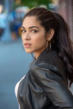 一位时尚女士在纽约市户外，穿着黑色皮夹克，戴着圆环耳环摆姿势