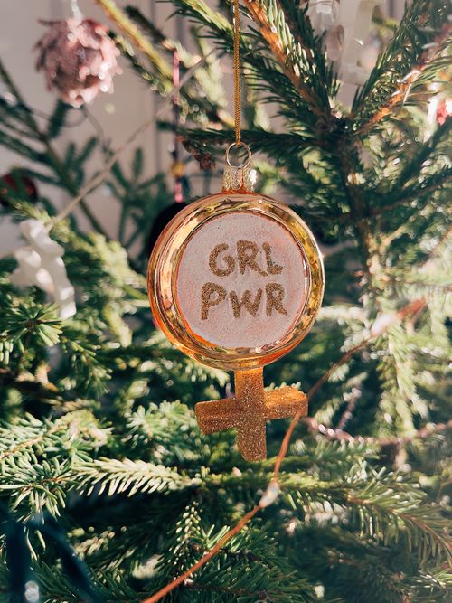 Free Gold 'GRL PWR' ornament hangs on a green Christmas tree, symbolizing empowerment. Stock Photo