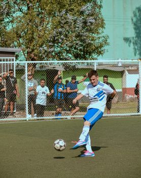 A soccer player in action kicking a ball on an urban outdoor soccer field during the day.