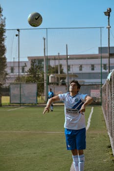 Teen soccer player in action, preparing to head the ball during a game on outdoor field.