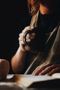 A woman enjoys coffee while baking bread in a warm, cozy kitchen.