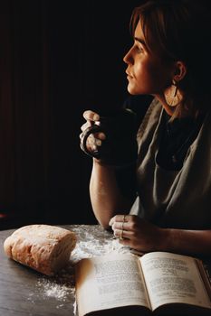 Woman enjoys coffee beside freshly baked bread, creating a warm kitchen vibe.