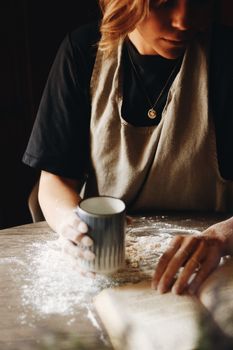 A woman baking bread while sipping coffee in a cozy kitchen.