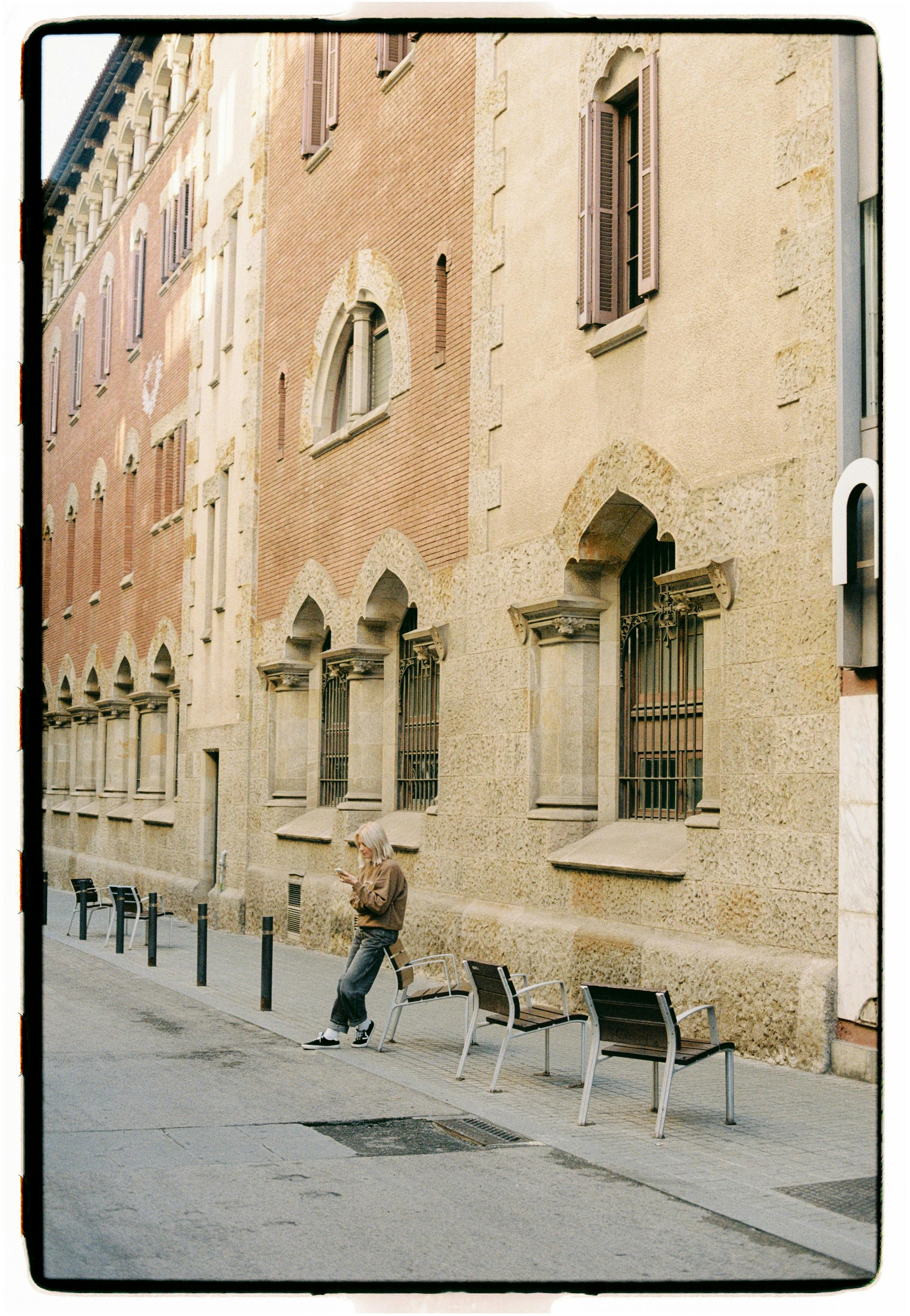 An adult man strolls past a historic building with stone and brick facade on a quiet street.
