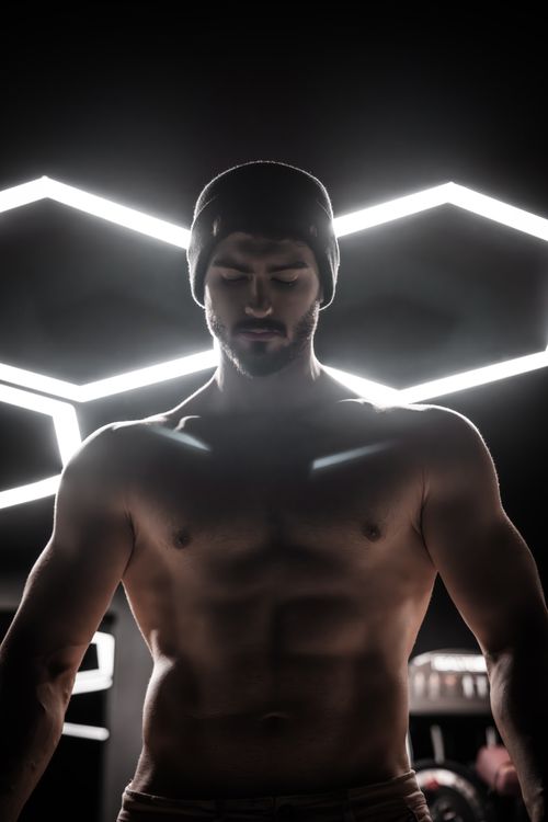 Free Muscular man wearing beanie under geometric gym lights, focused expression. Stock Photo