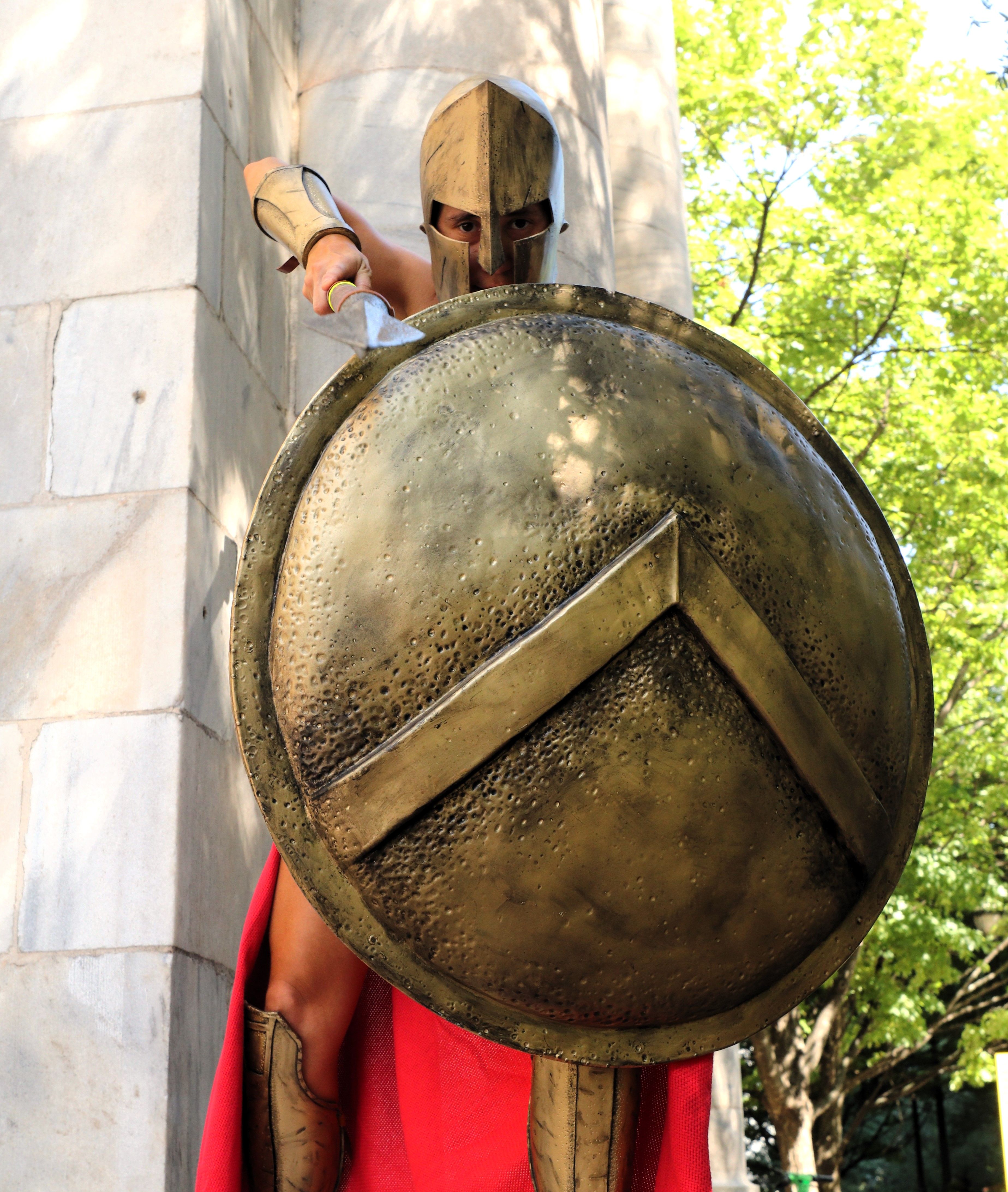 A Spartan warrior in armor holding a shield outdoors on a sunny day.