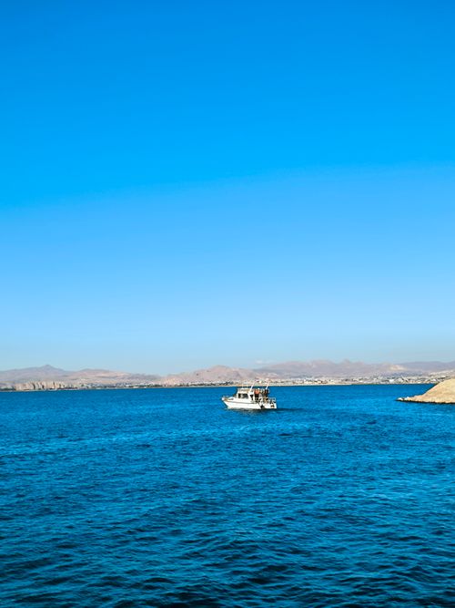 Free A peaceful lake scene featuring a solitary boat under a vibrant blue sky. Stock Photo