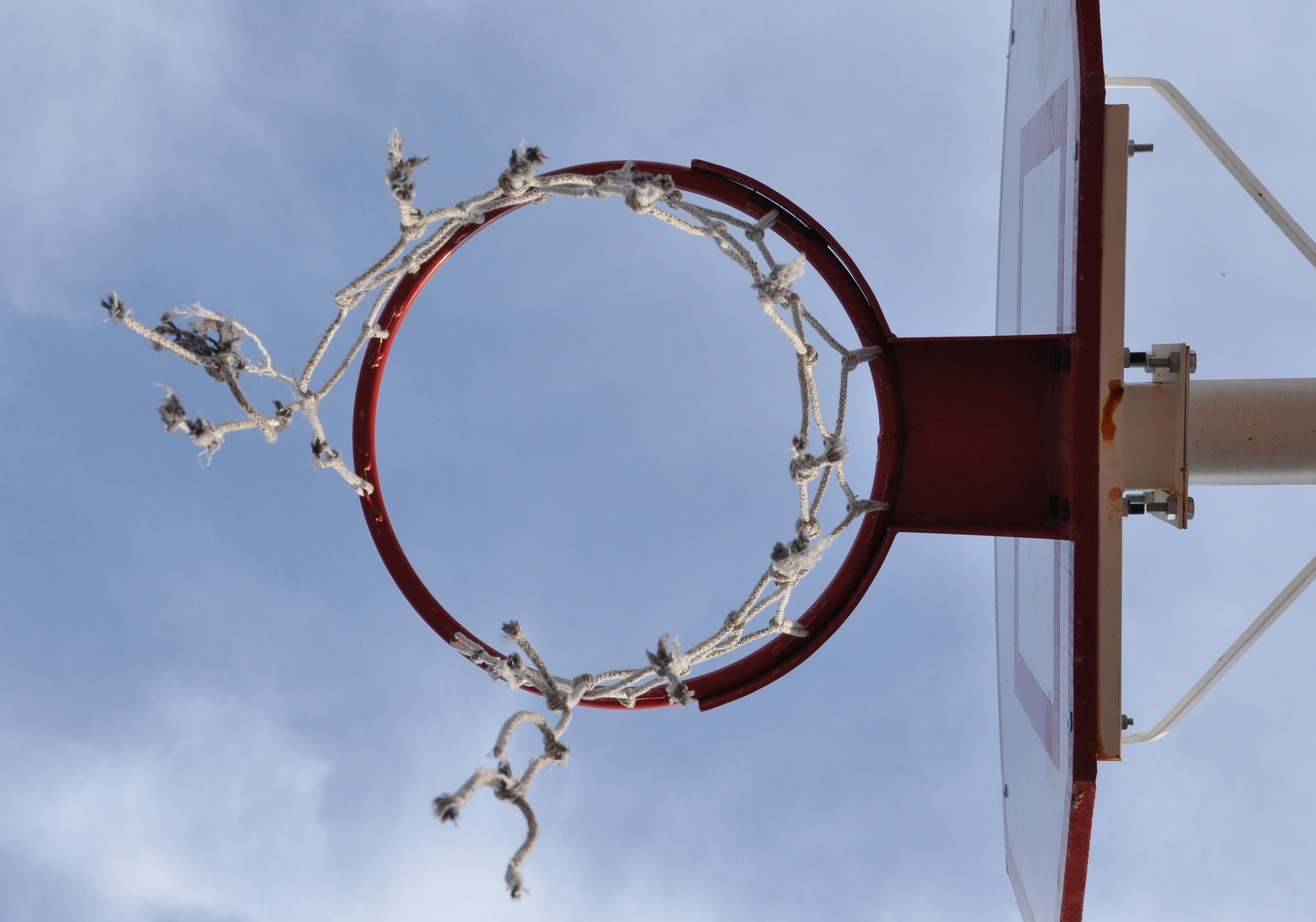 Basketball hoop with tattered net against a clear sky, conveying a sense of unused time.