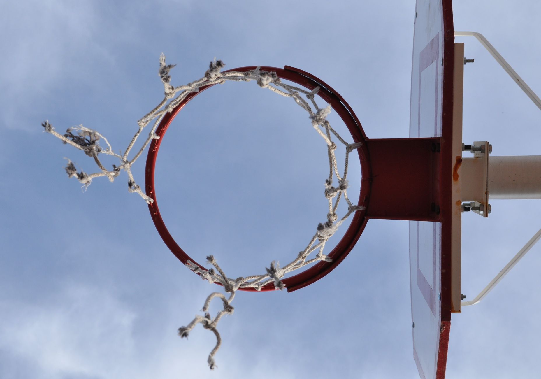 Basketball hoop with tattered net against a clear sky, conveying a sense of unused time.