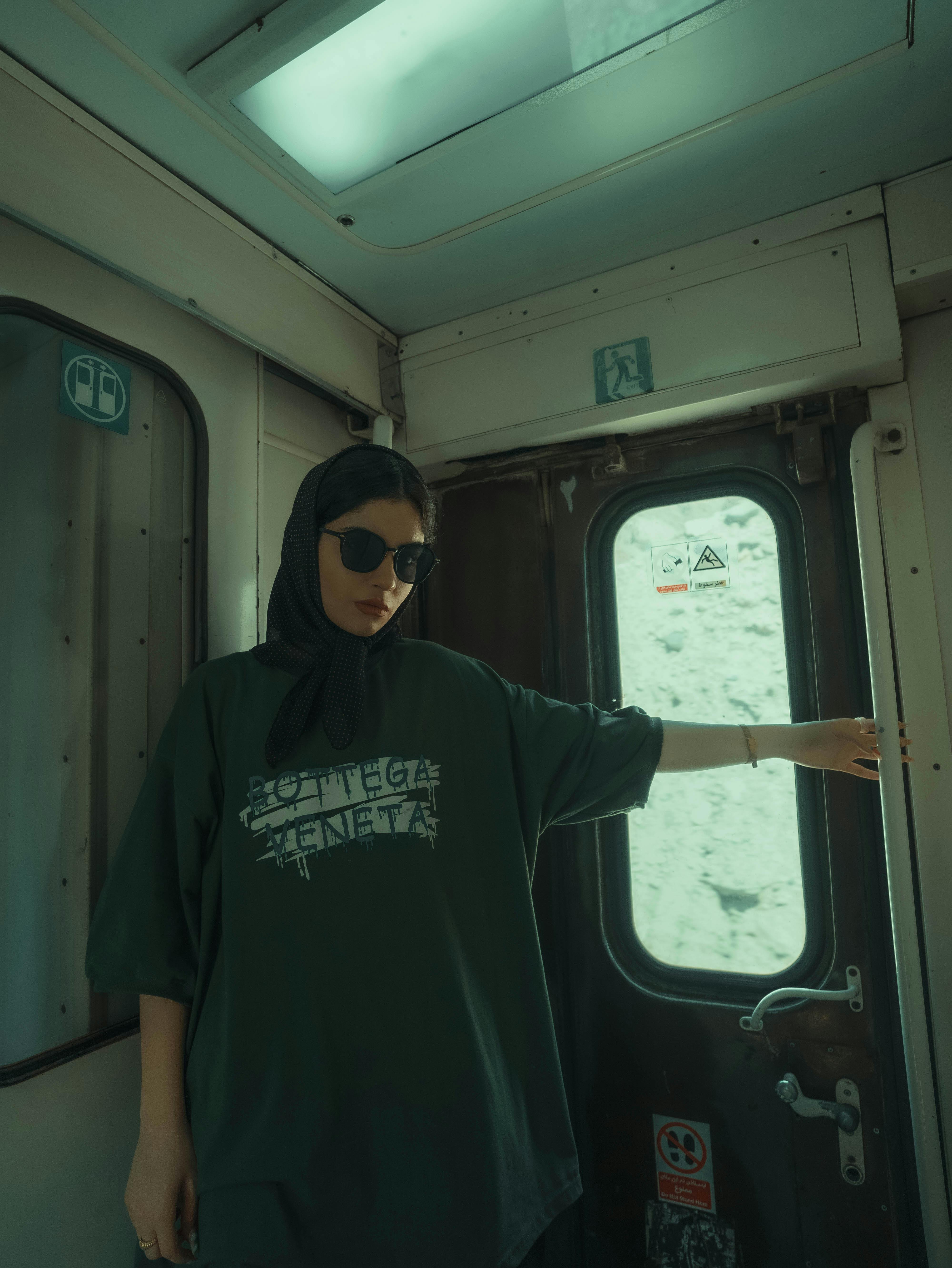 Free Woman in dark clothing on train, wearing sunglasses and hijab, with graffiti-inspired design on shirt. Stock Photo