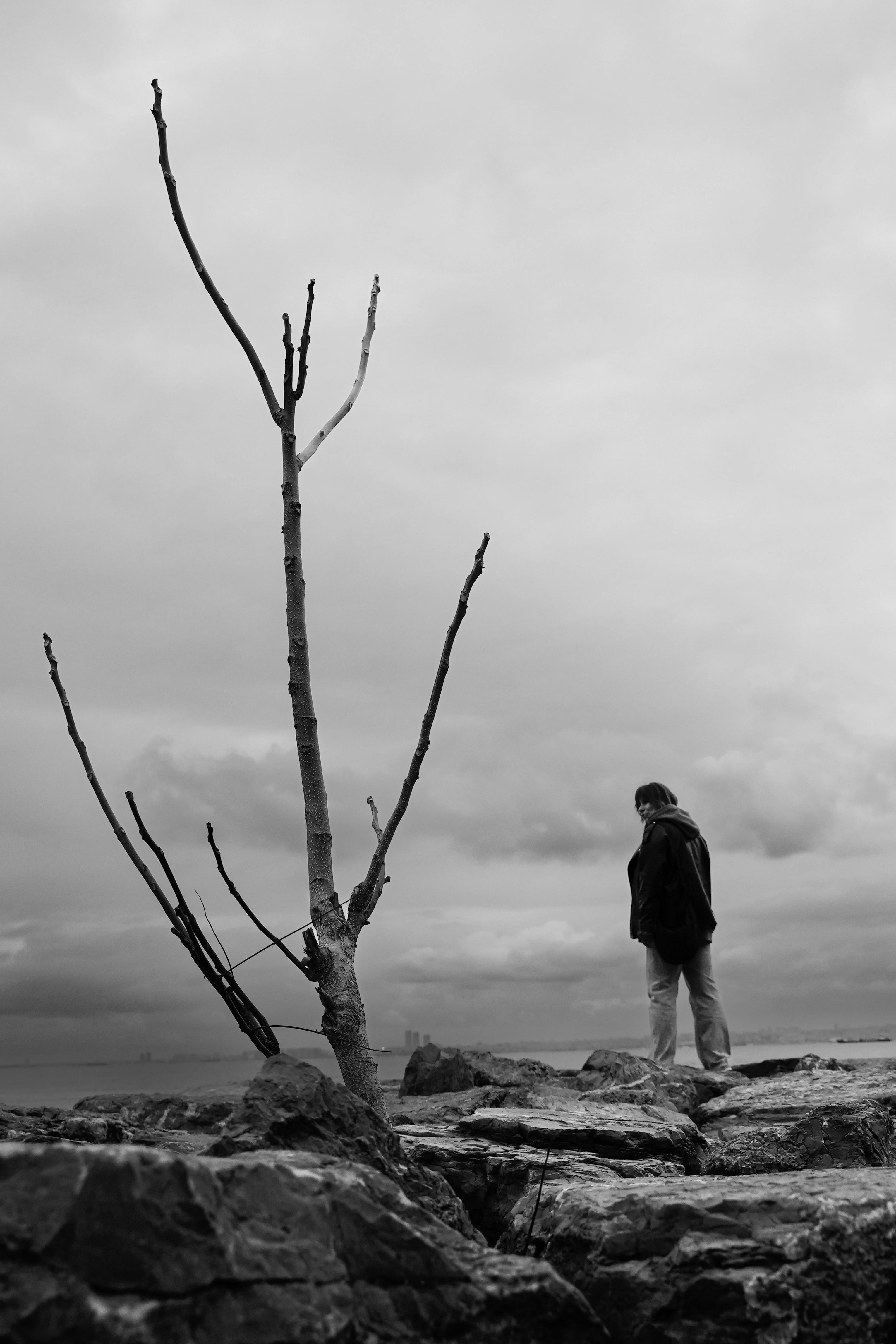 A solitary person stands on rocky coast in Istanbul, exuding a moody atmosphere.