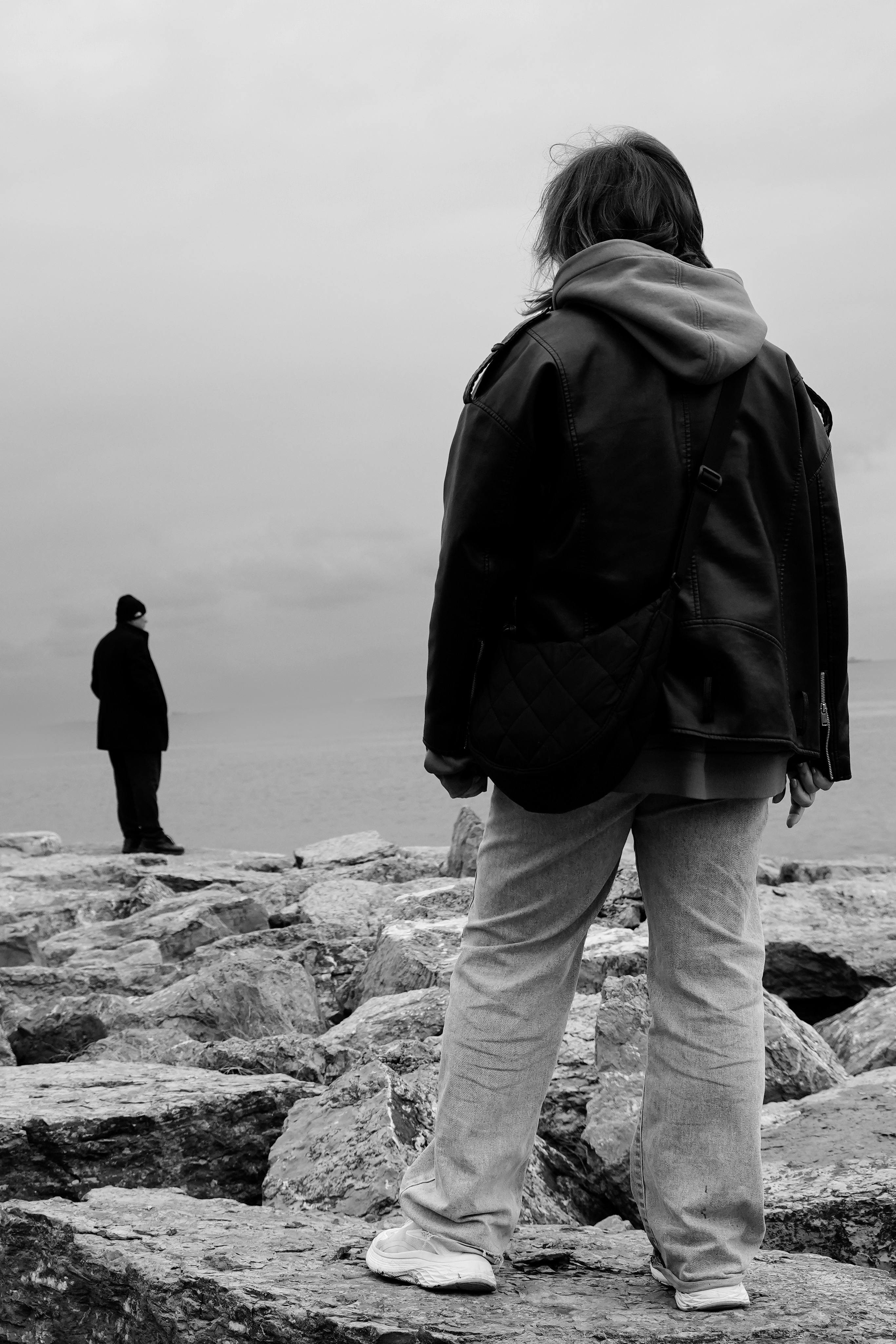 Dramatic black and white photo of two people at a rocky shore in İstanbul, capturing a mood of solitude and reflection.