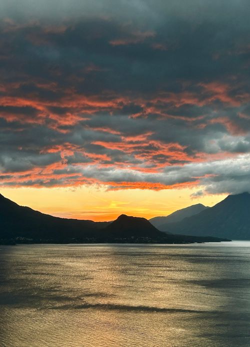 Free A stunning sunset with dramatic clouds over a peaceful lake surrounded by volcanoes. Stock Photo