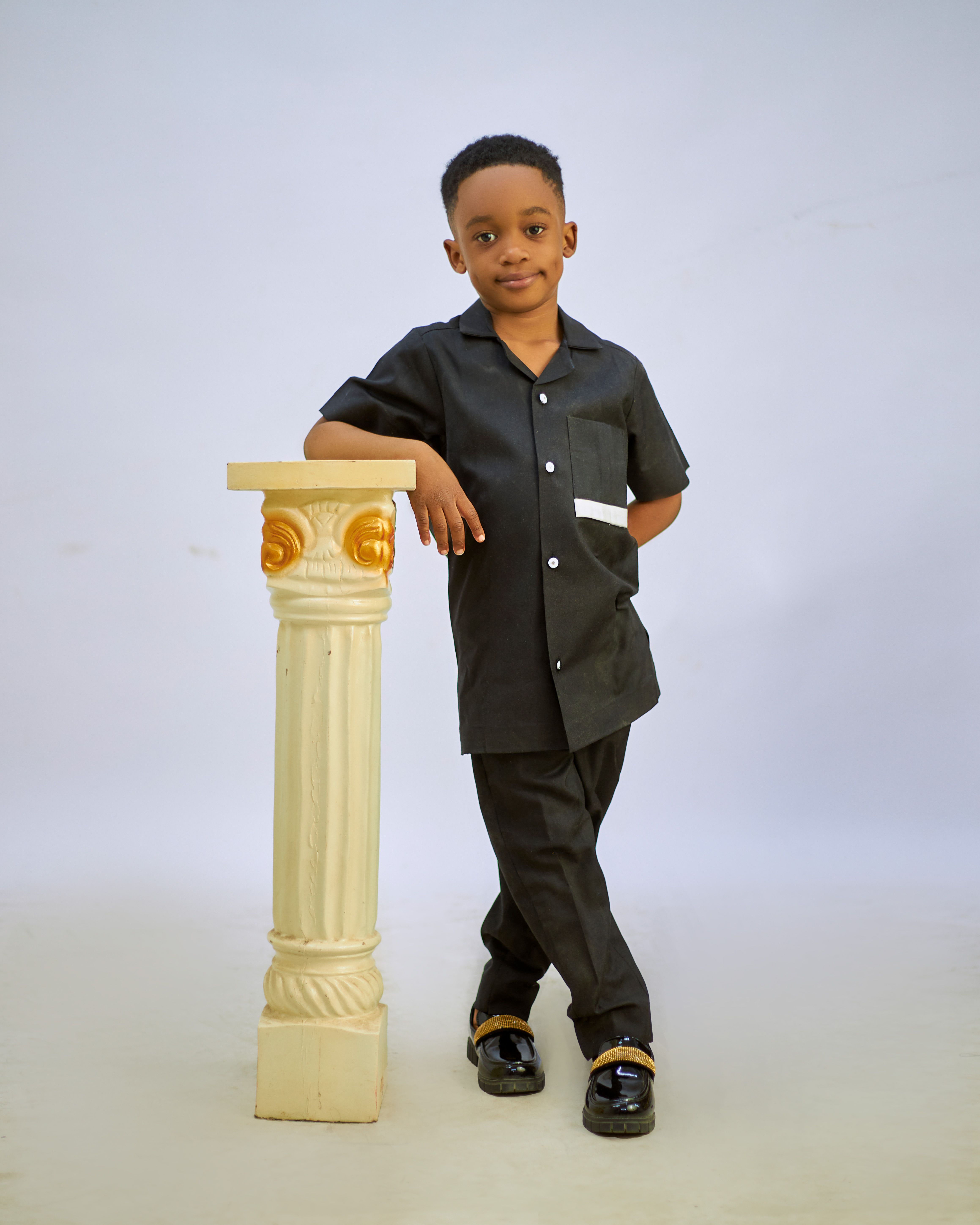 Portrait of a young boy in smart attire posing by a decorative column.