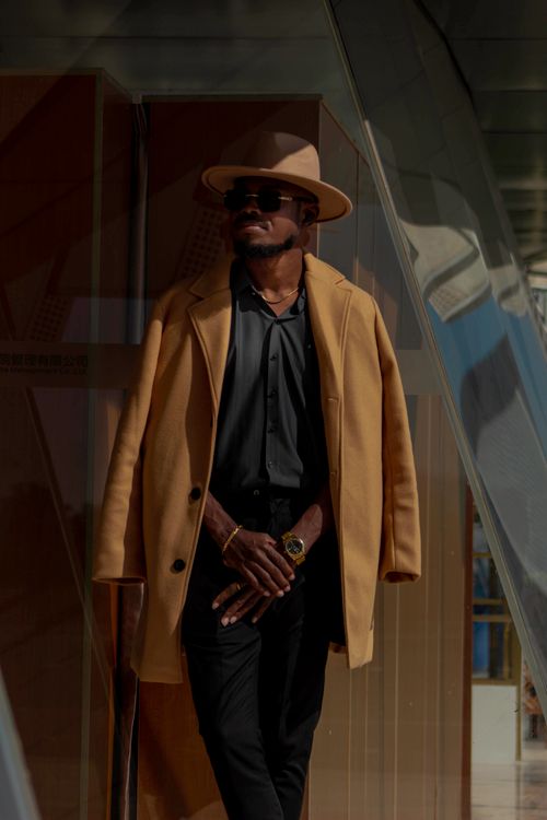 Free Elegant man wearing hat and coat stands confidently outdoors with modern reflections. Stock Photo