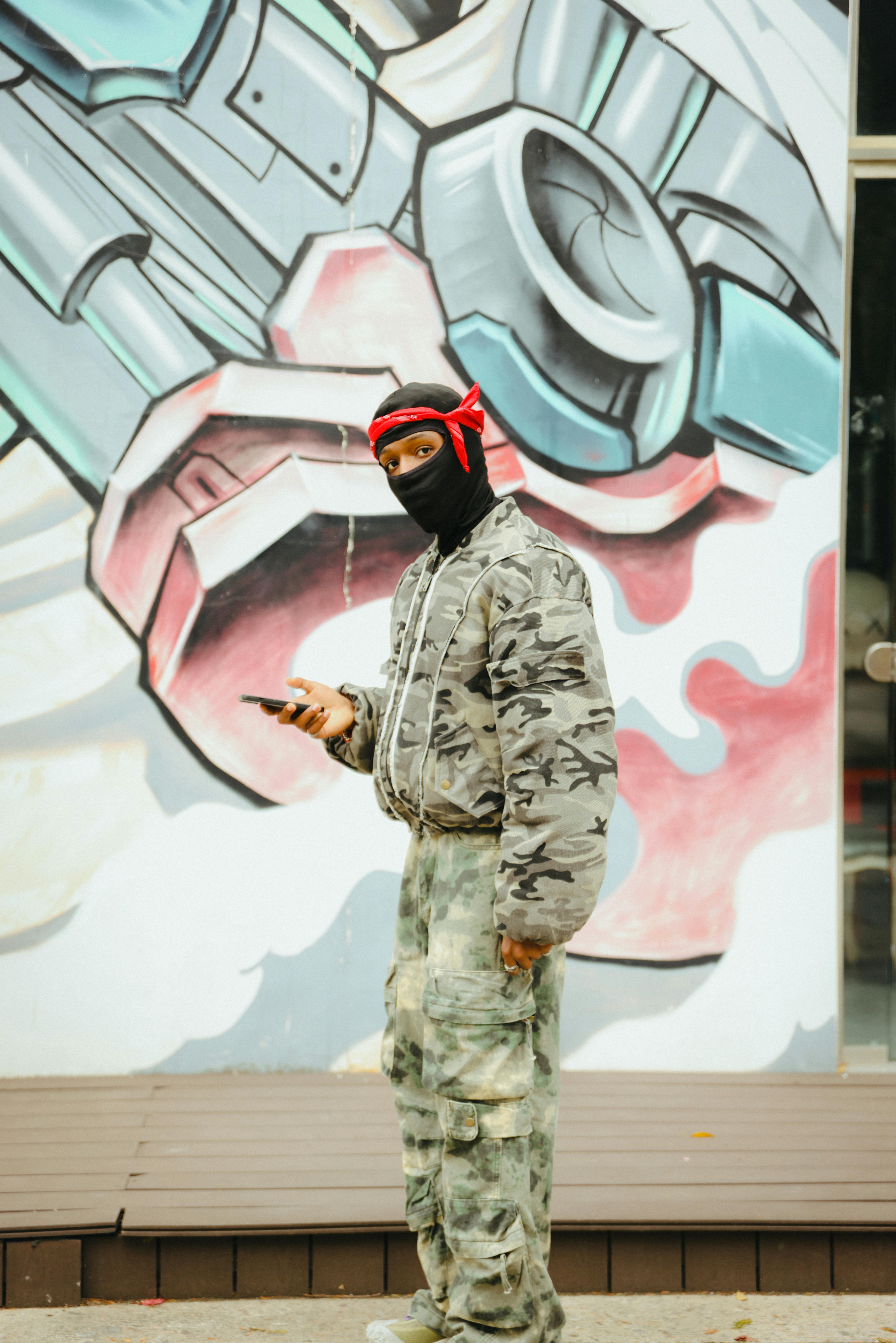 Masked Individual in Camouflage by Urban Graffiti · Free Stock Photo