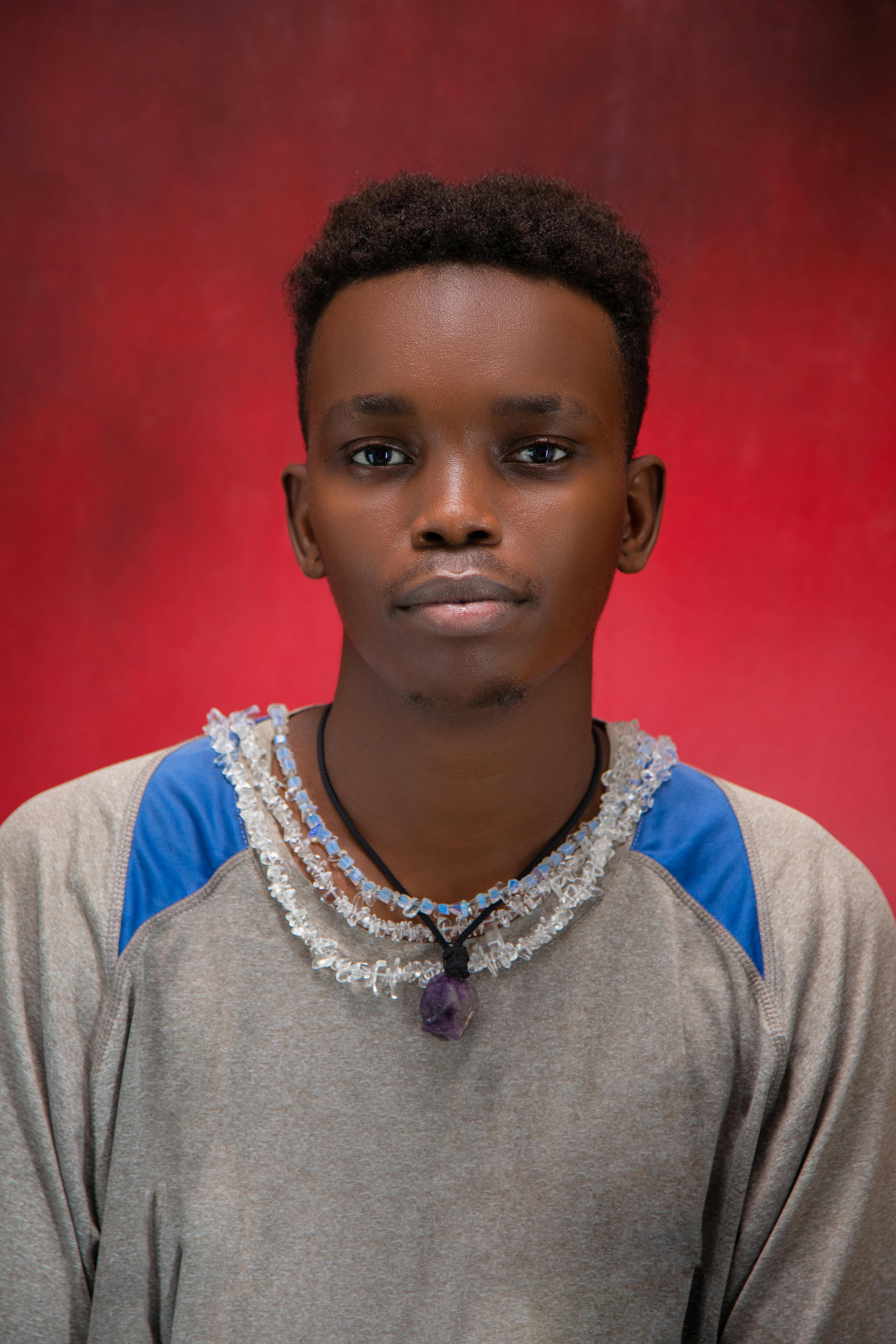 Expressive portrait of a young man against a vibrant red background, wearing a casual outfit and necklace.