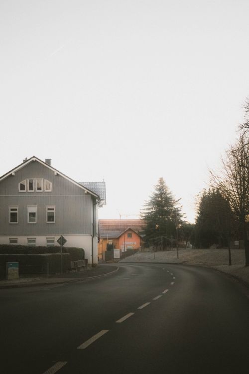 Free Peaceful countryside road at dusk with houses and trees, creating a calm atmosphere. Stock Photo