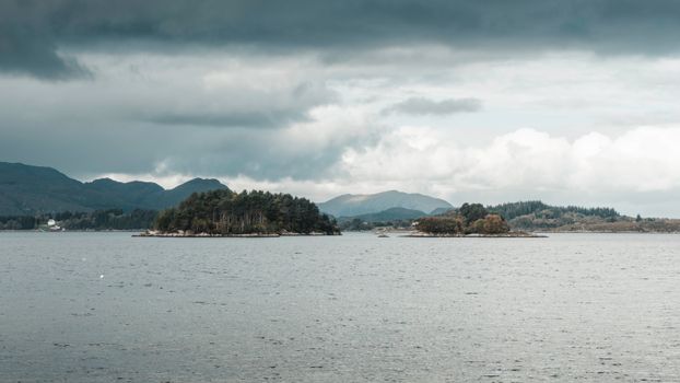 Peaceful view of Norwegian fjord and small islands under dramatic overcast sky.